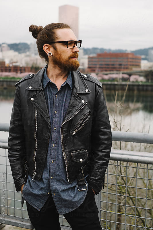Hip man with red facial hair standing with bridge and cityscape