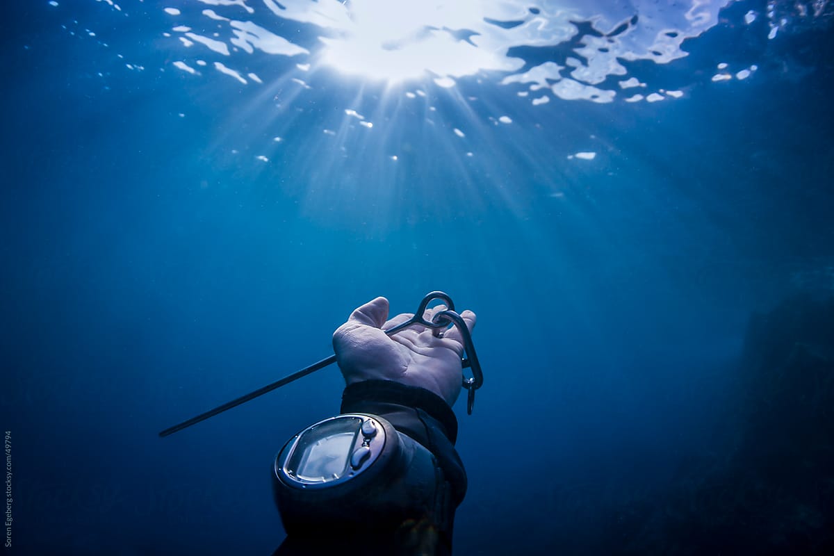 Divers hand with pointer stick and dive computer reaching out to sun light underwater in the ocean