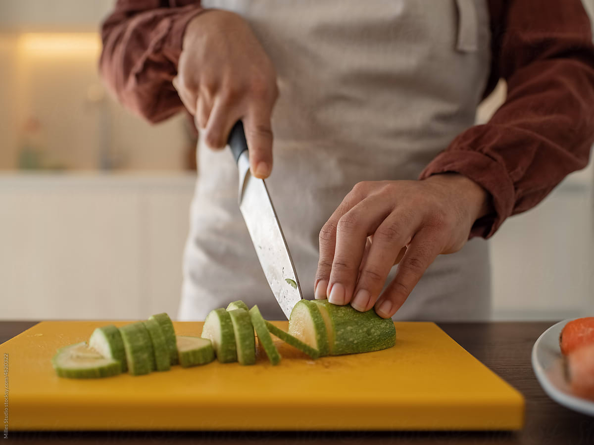 Crop female slicing zucchini on board