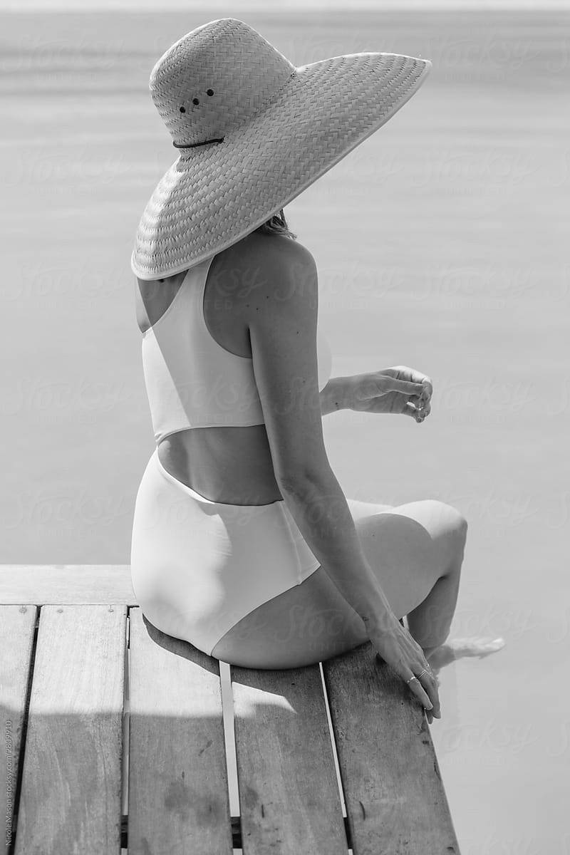 Young Woman In White Swimsuit And Large Sun Hat Sitting By The Edge Of A  Pool by Stocksy Contributor Nicole Mason - Stocksy