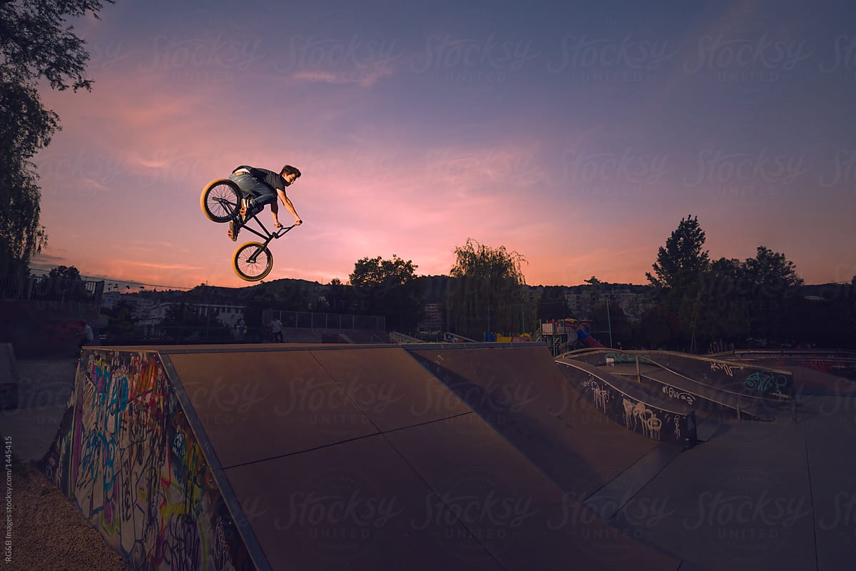 Teenager performing midair stunts with BMX against dramatic twilight sky