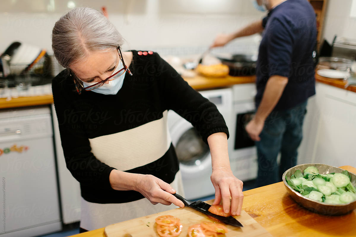 Elderly woman with a face mask cooking in home kitchen