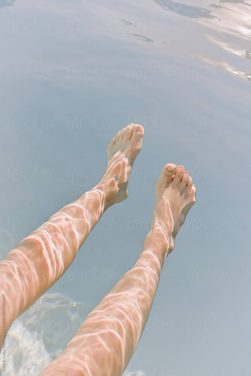 Adult woman's legs in a pool with the water reflection