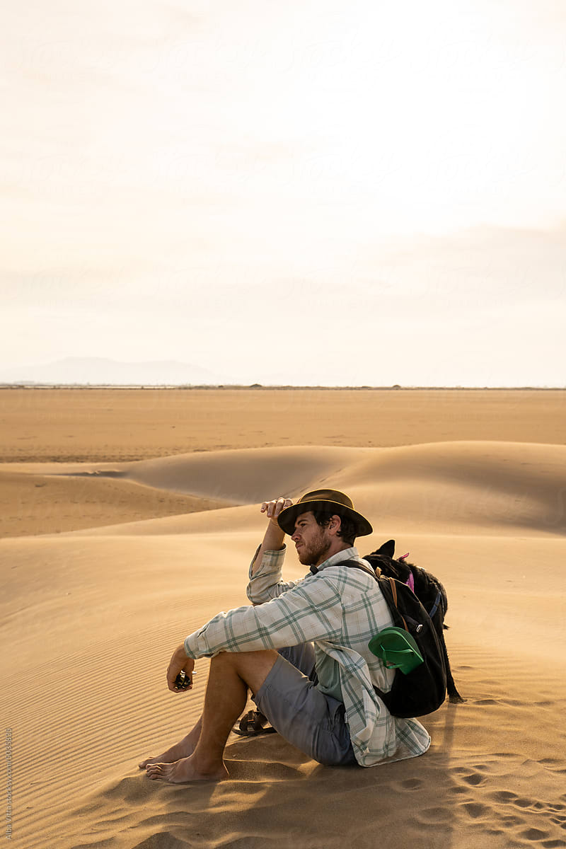 Man sitting on top of dune in desert