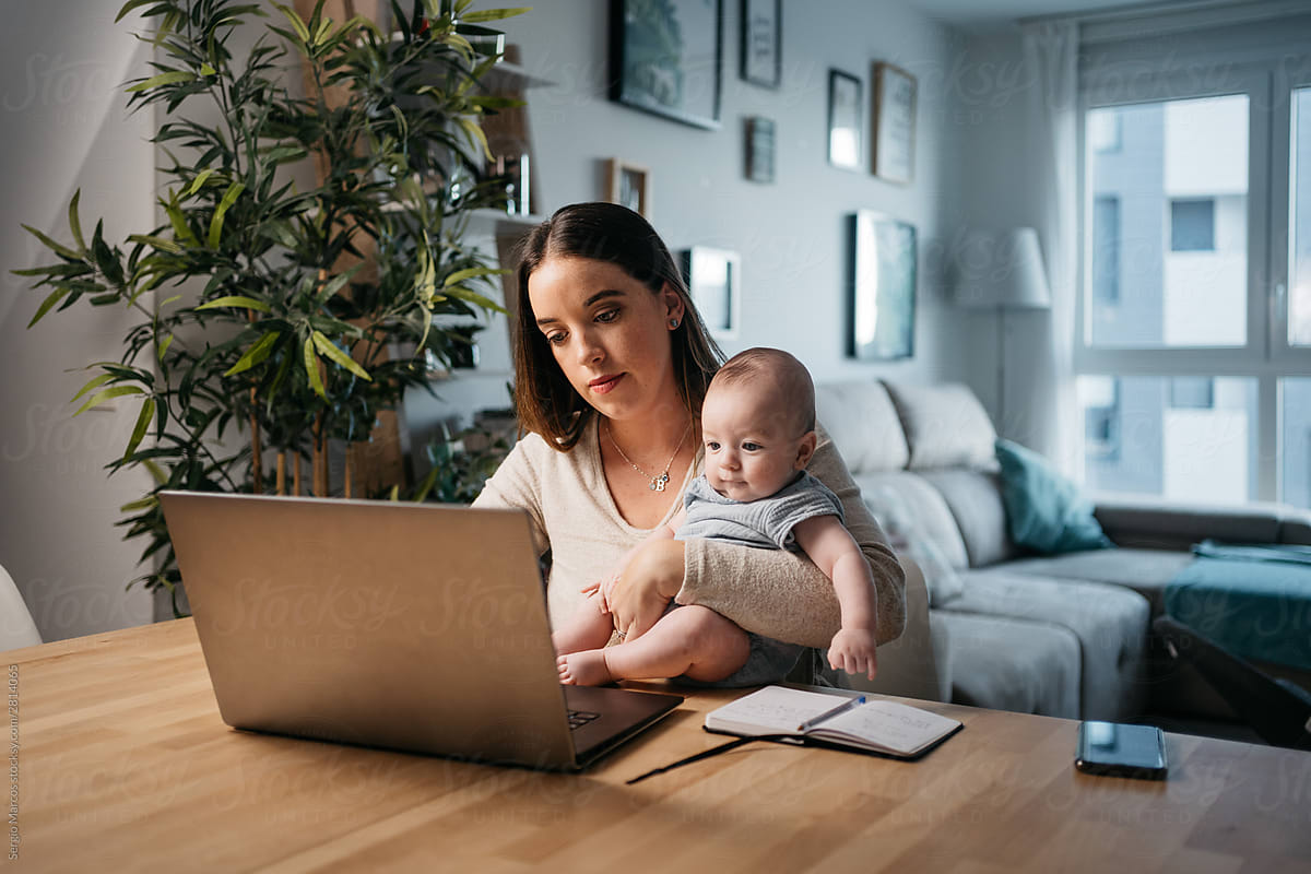 Young woman taking care of her baby while working at home