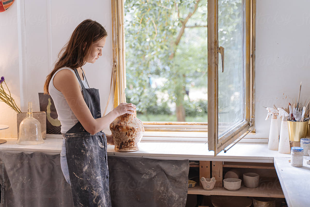 Female potter creating vase near window