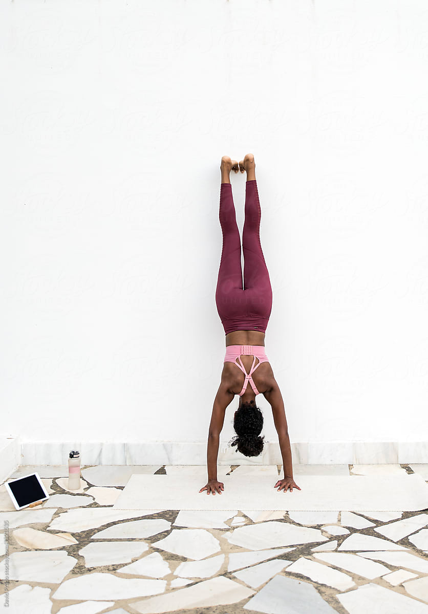 Anonymous ethnic female doing handstand near wall