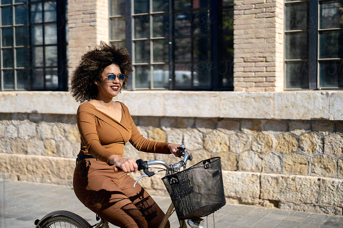 Joyful black woman riding bicycle in city