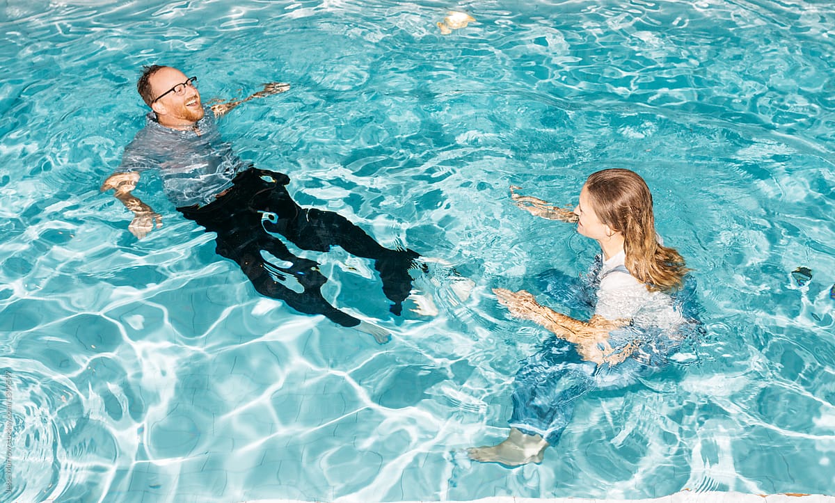 Couple laughing while swimming with all their clothes on during spontaneous summer pool party