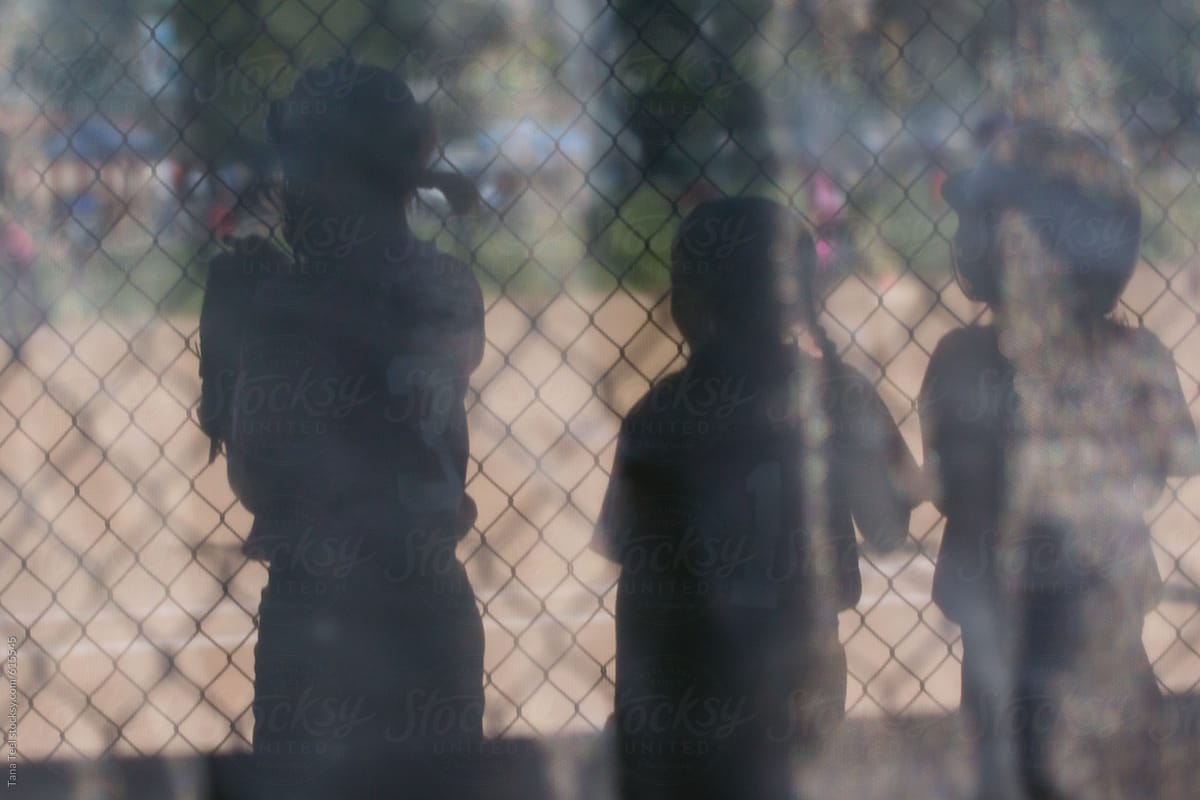 Three softball players standing inside dugout during game