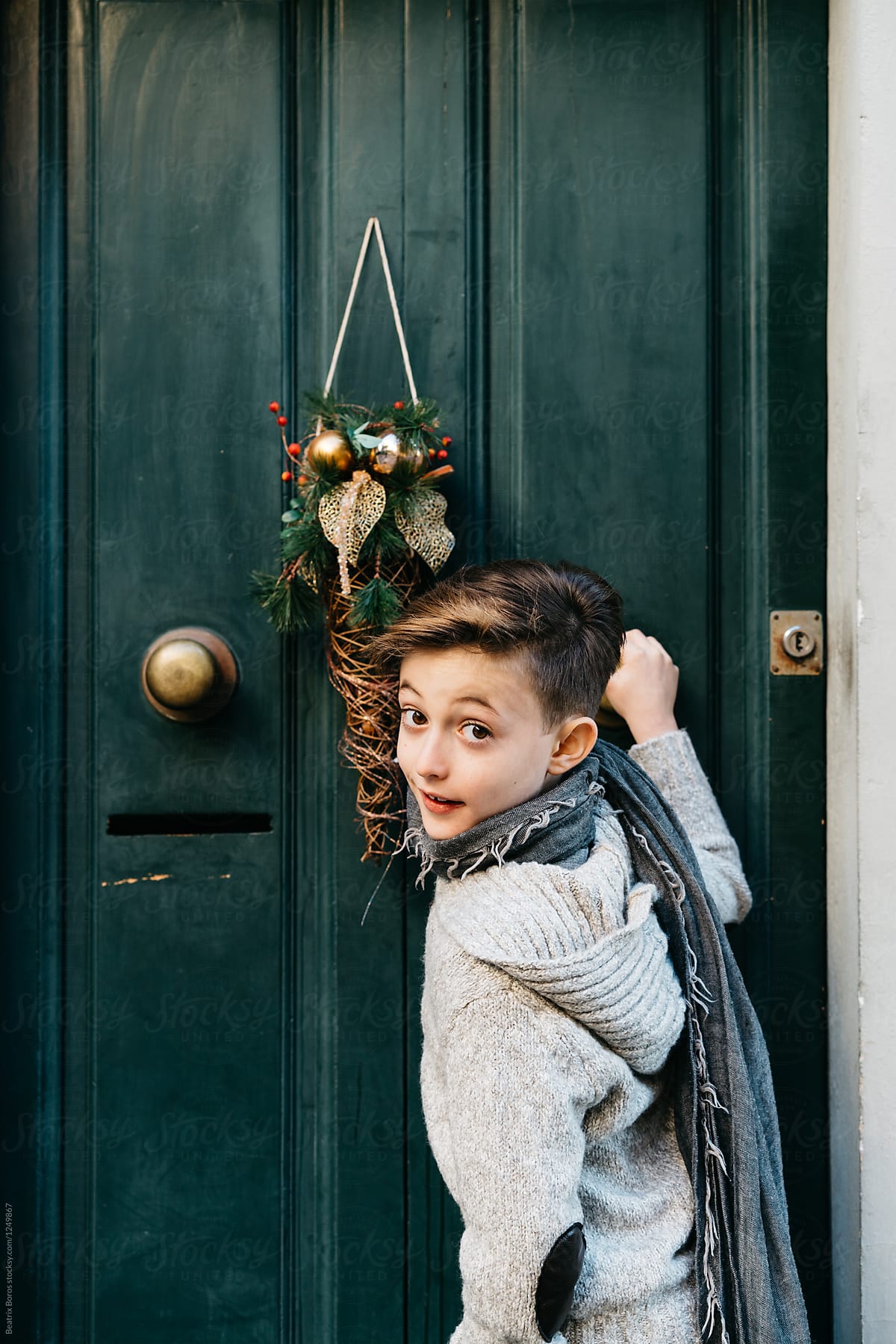 Boy knocking on a decorated door, while curiously looks back to camera