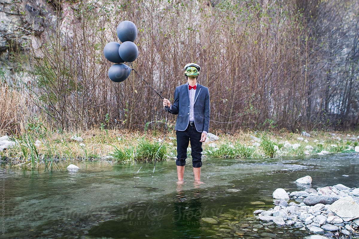 Man Wearing Creepy Frog Mask and Black Balloons in Stream