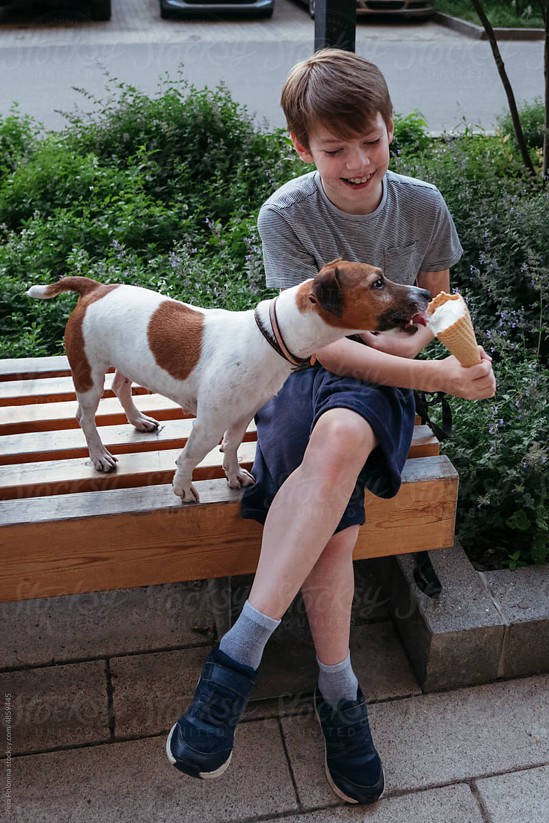 Kid shares ice cream with pet dog.