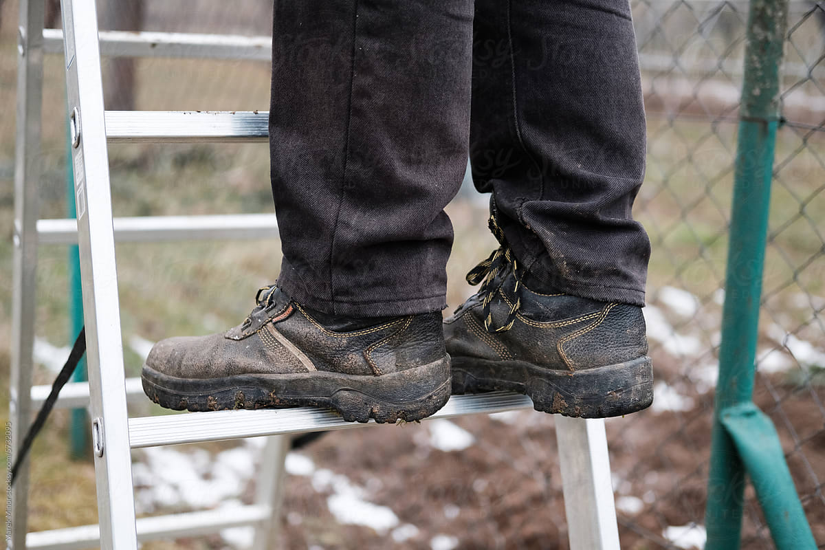 Closeup of man\'s legs with old worker shoes standing on a ladder