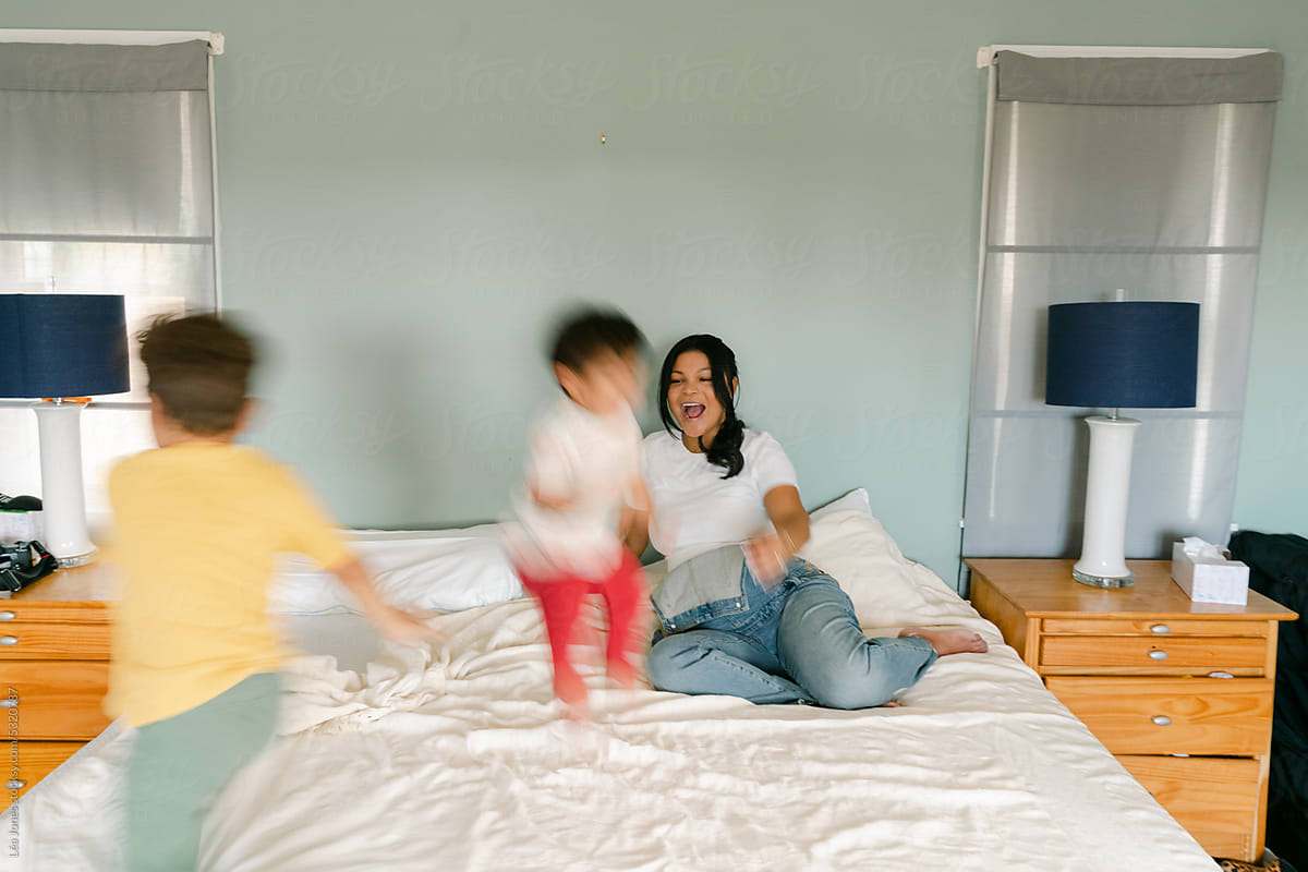 pregnant mother playing on bed with her toddlers