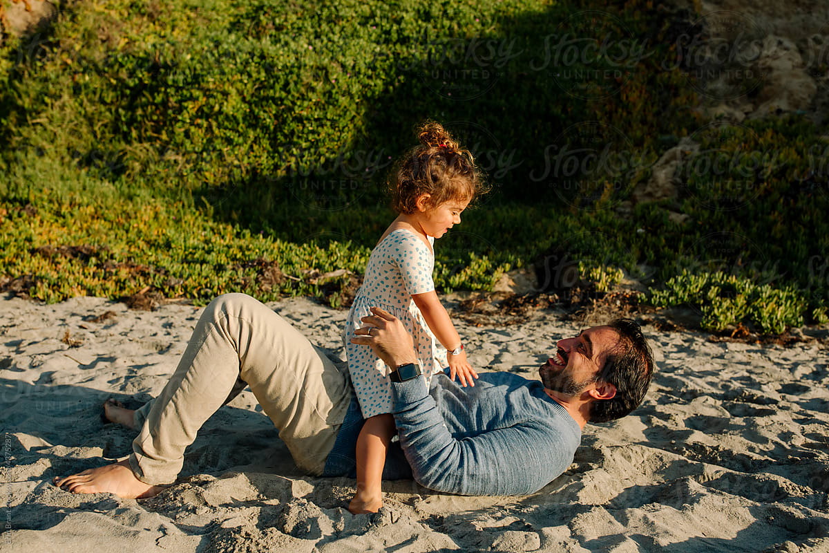 Dad lying on back with daughter at beach