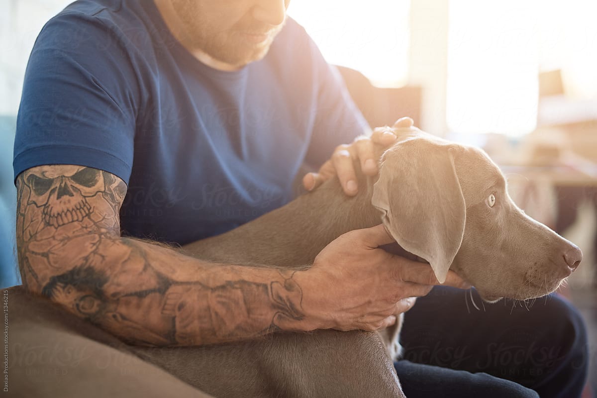 Hipster man with tattoos stroking his pet dog
