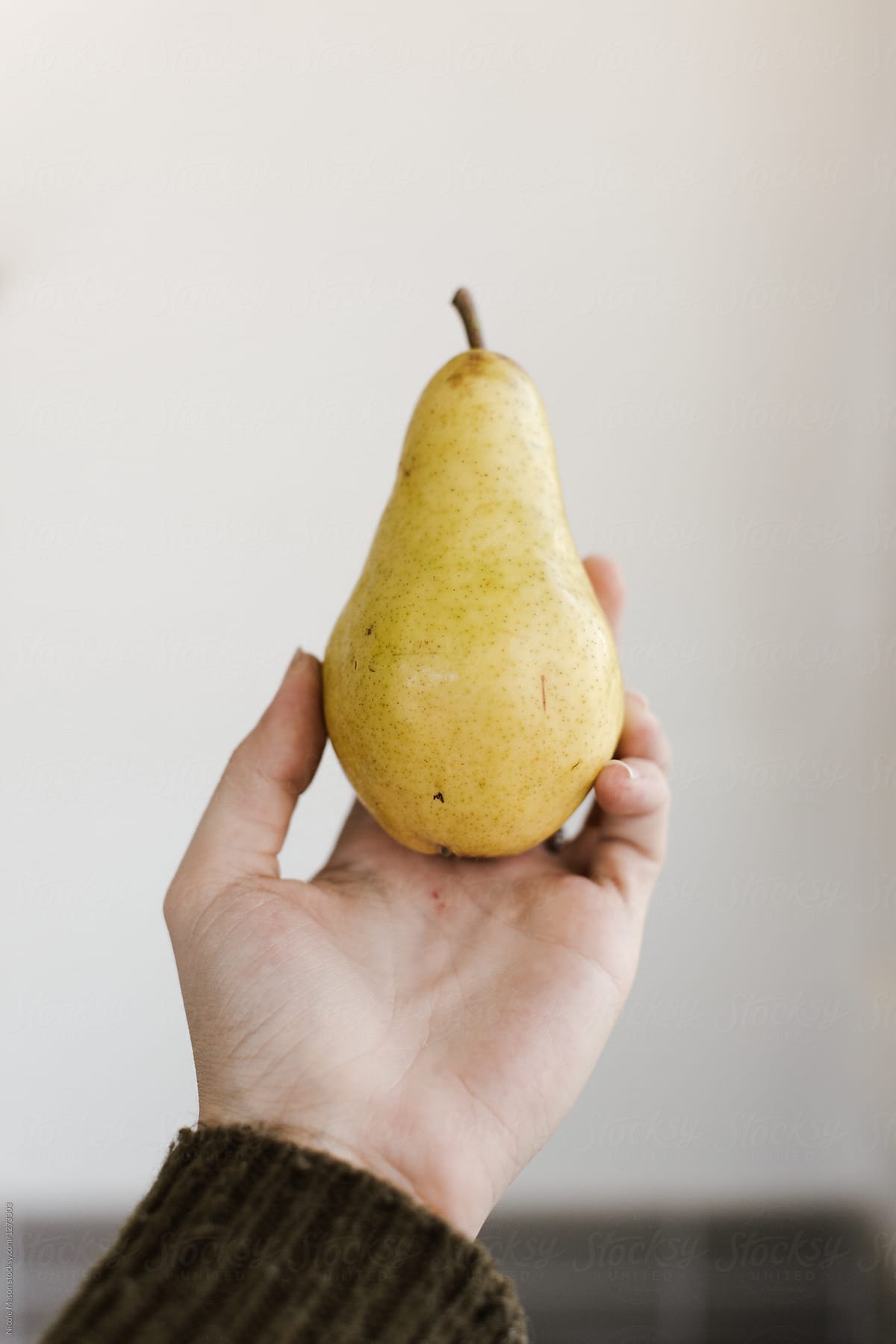 hand holding a pear in front of white wall