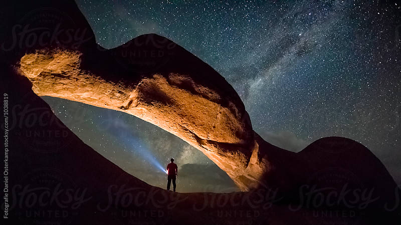 Person under a stone arch lighting up the milky way