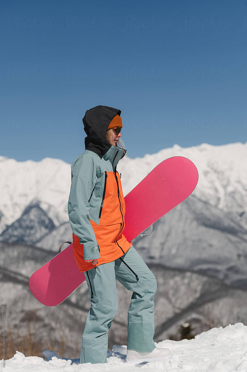 Athletic lady with snowboard standing on snowy terrain