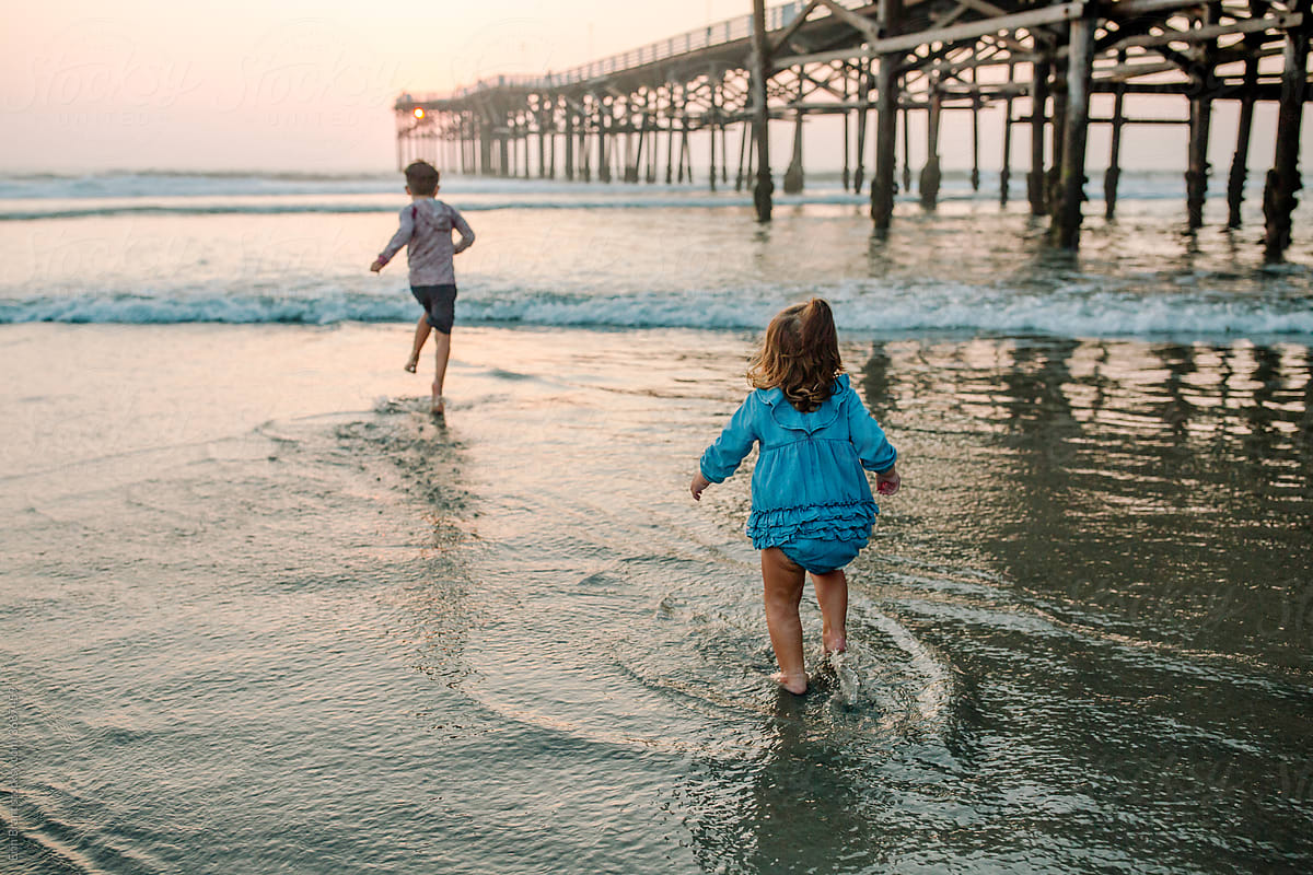Young siblings running in the ocean at sunset
