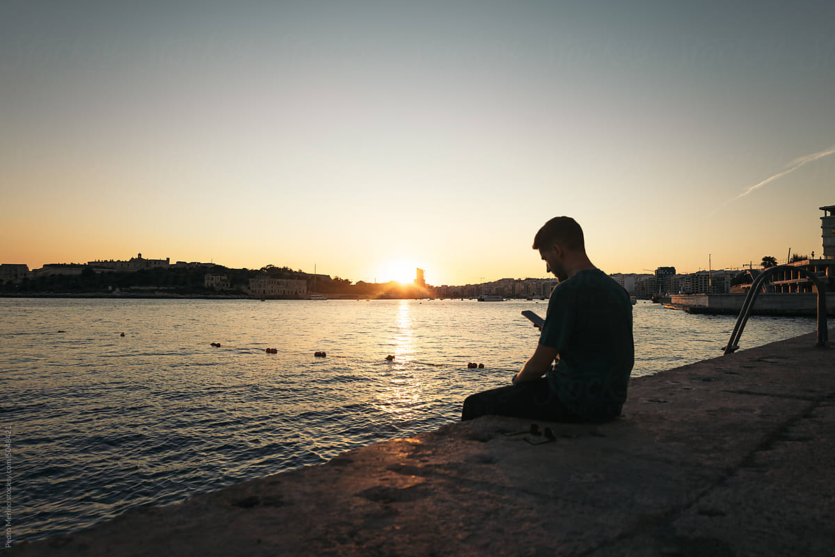 Young man watching the sunset in Valletta, Malta and using smartphone