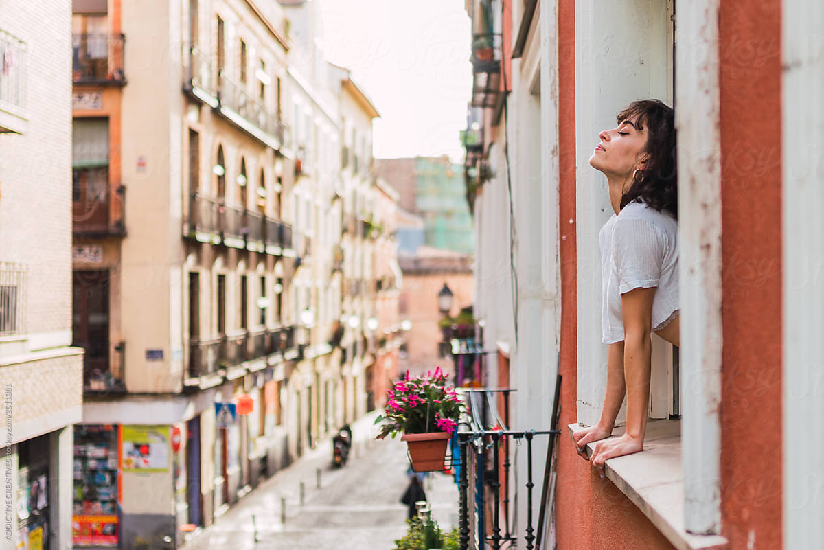 Cheerful Young Woman Leaning Out Of Window By Addictive Creatives