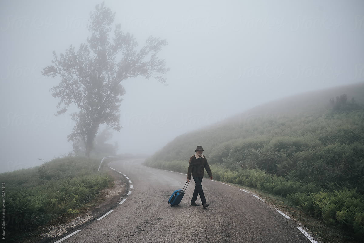 a man with luggage on an empty rural  road