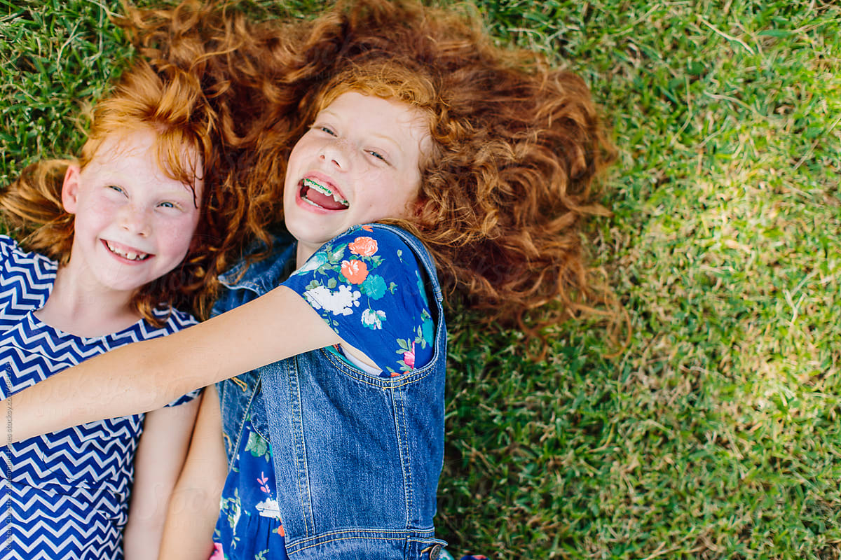 Two adorable red headed sisters having fun outdoors on the grass / lawn