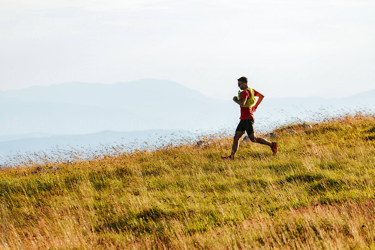 Man Running In The Field With Mountain Range In Background.