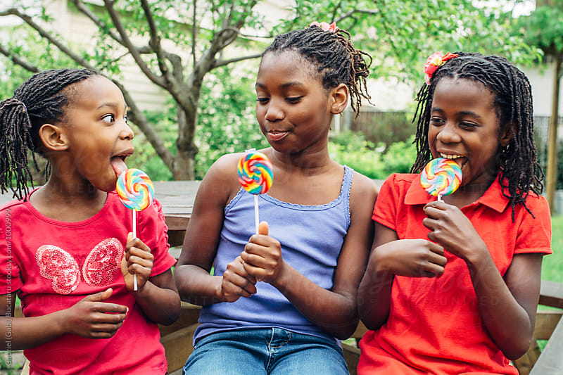 Three black girls on a bench with lollipops