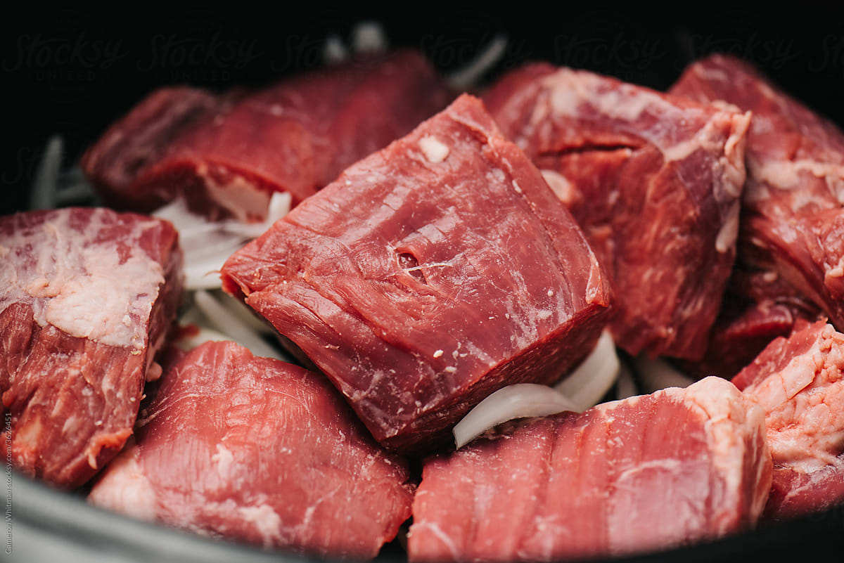 Raw cuts of beef flank steak with onions in a slow cooker