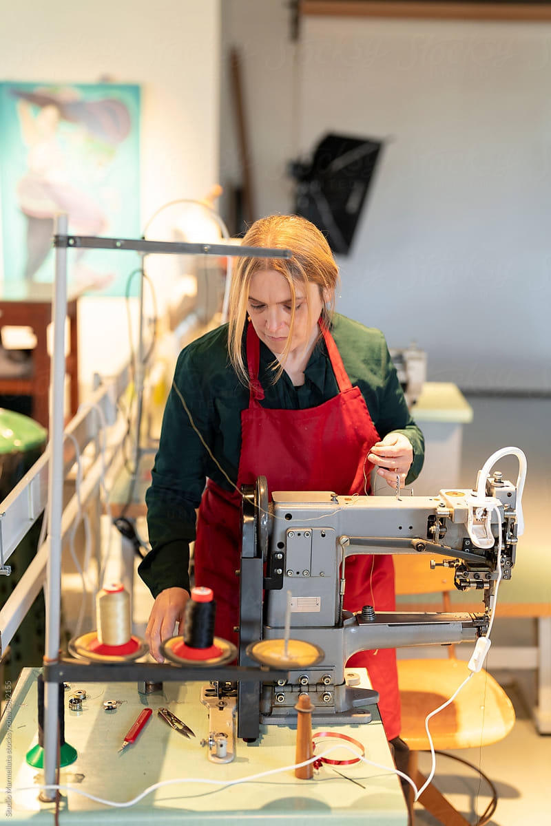 Focused woman working on sewing machine under lights in workshop
