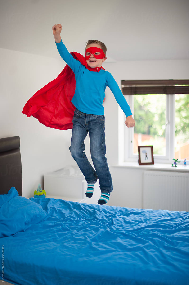 boy in superhero costume jumping on his bed