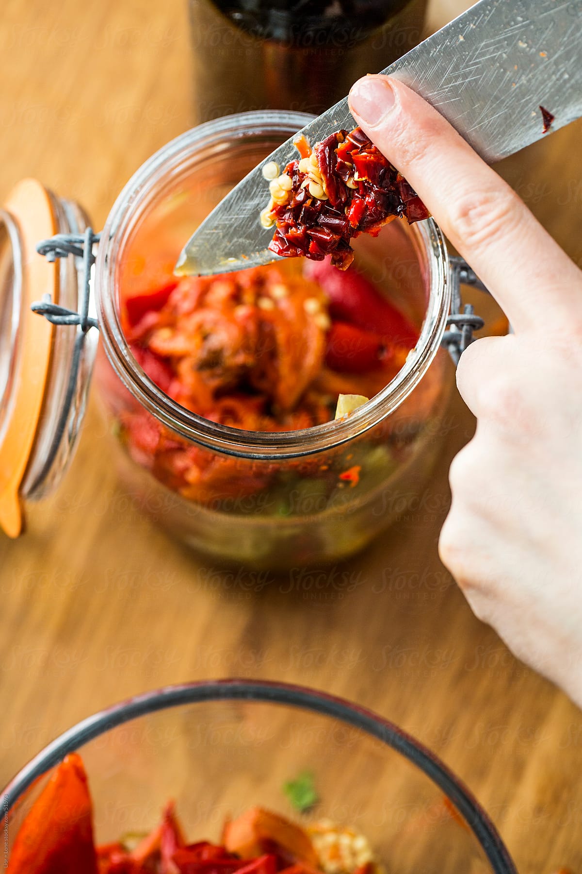 finger sliding chopped chilies into glass jar