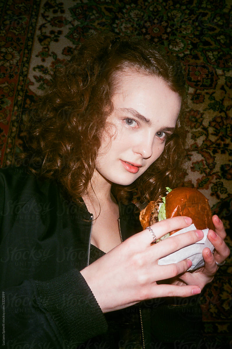 Girl  dressed in black looking to the camera with a delicious burger