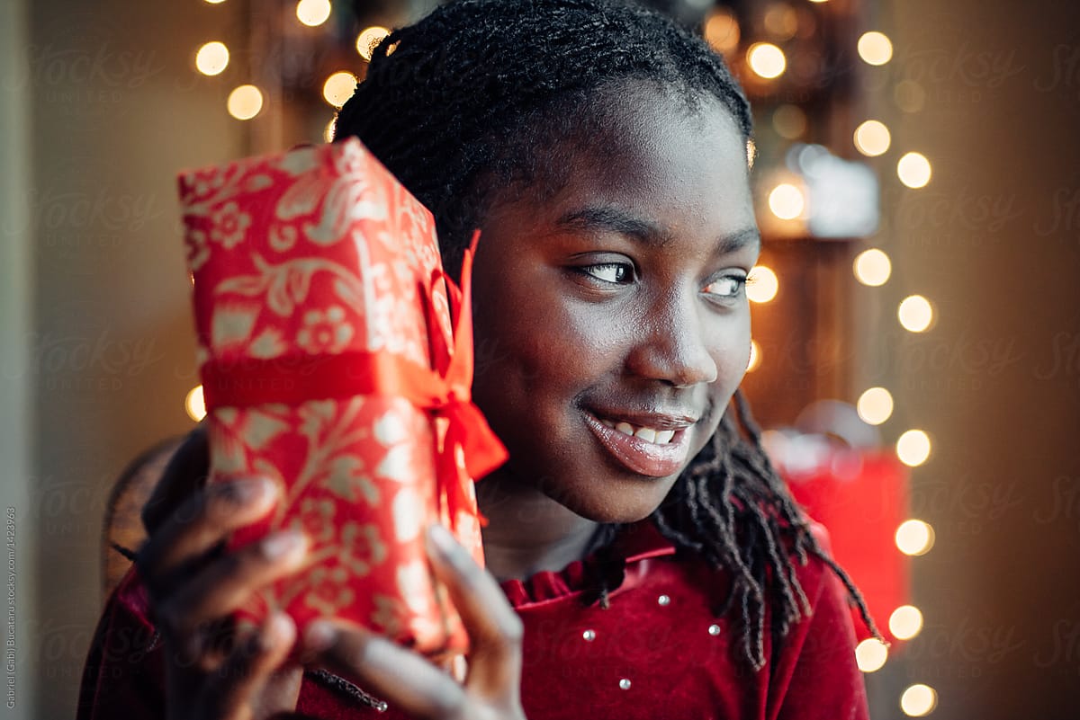 Black girl shaking a Christmas gift to hear what\'s inside
