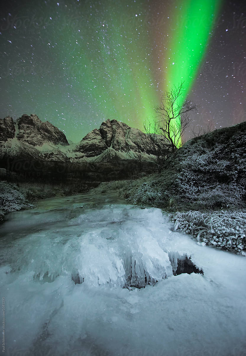 Frozen creek and Snow covered mountain range under northern lights