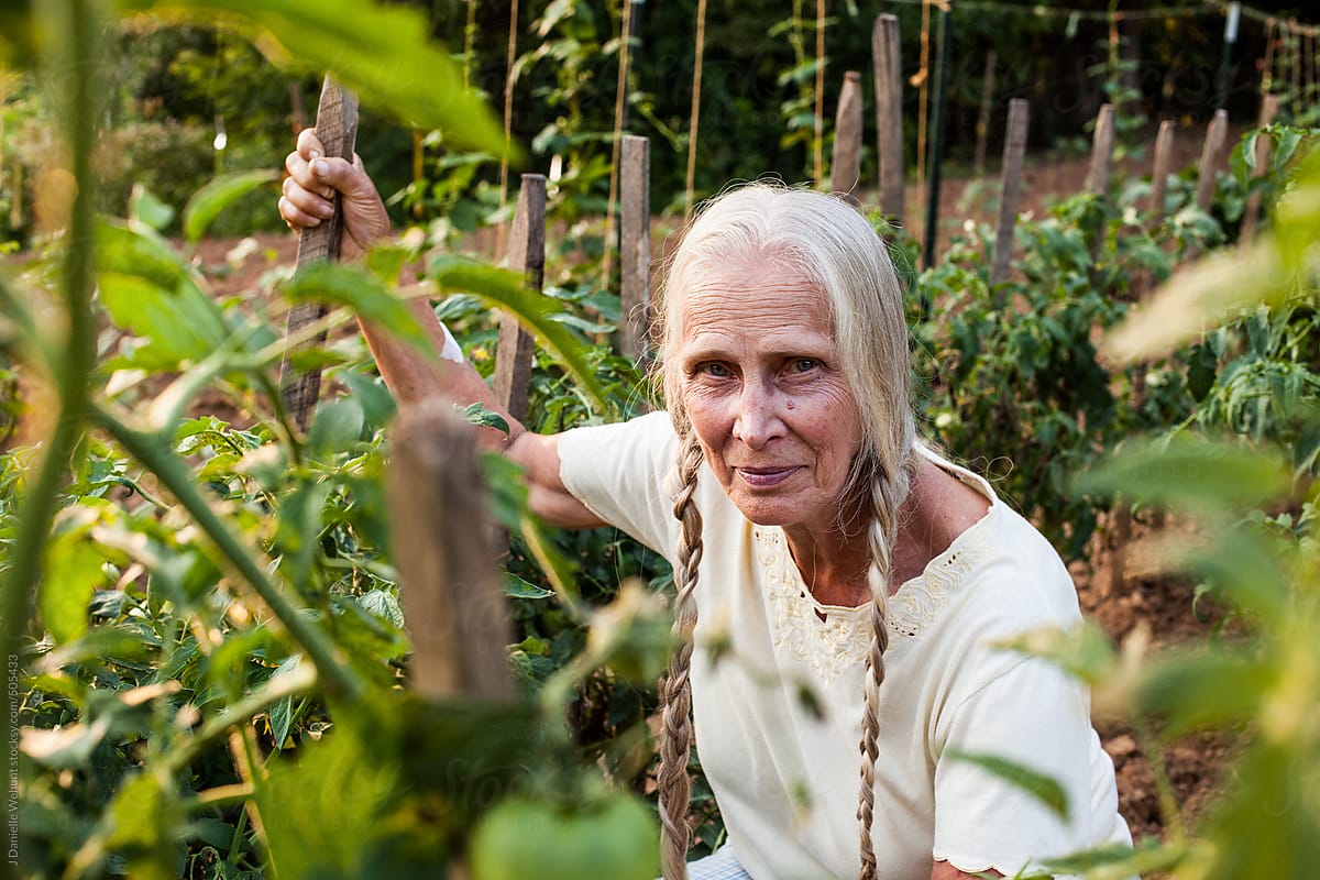 Elderly blonde woman with braids sitting in a vegetable garden row