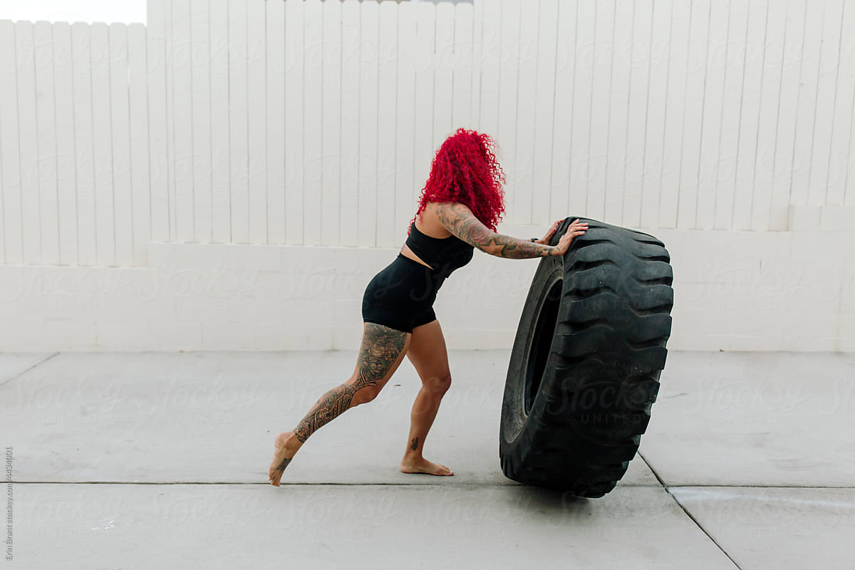 Strong woman with red hair pushing tire