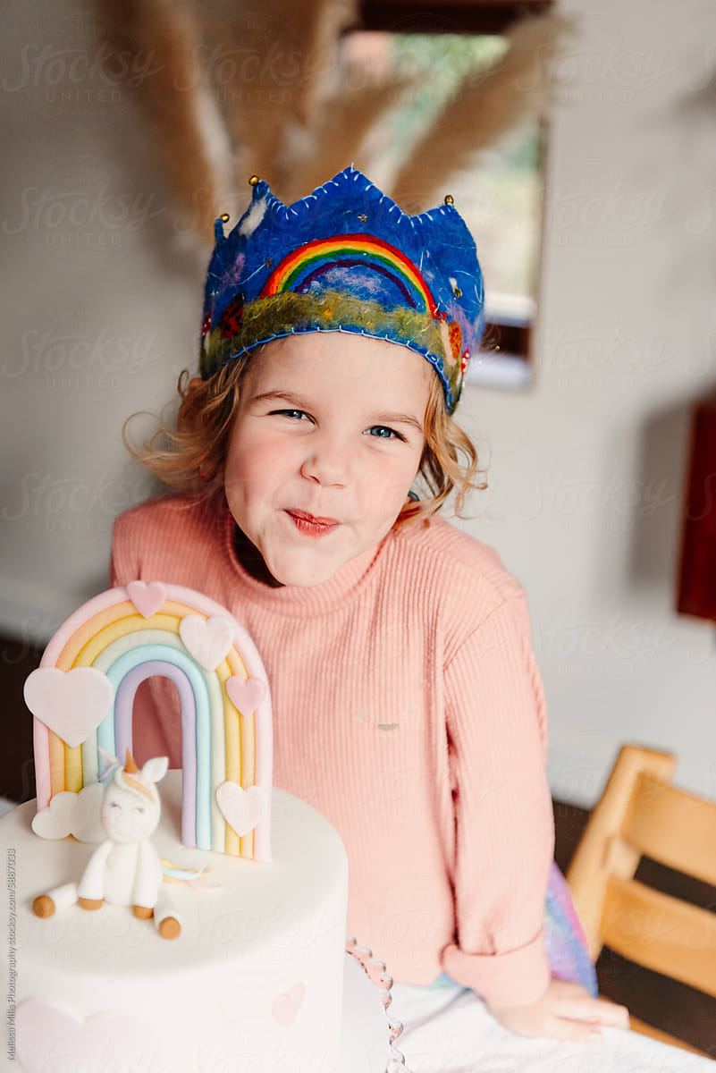 Girl with unicorn and pastel rainbow themed bday cake at home party
