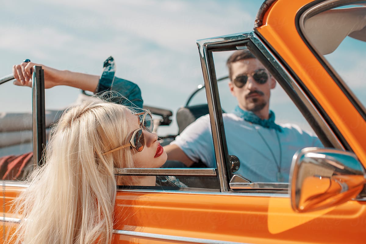 Attractive couple in orange retro car on a road trip