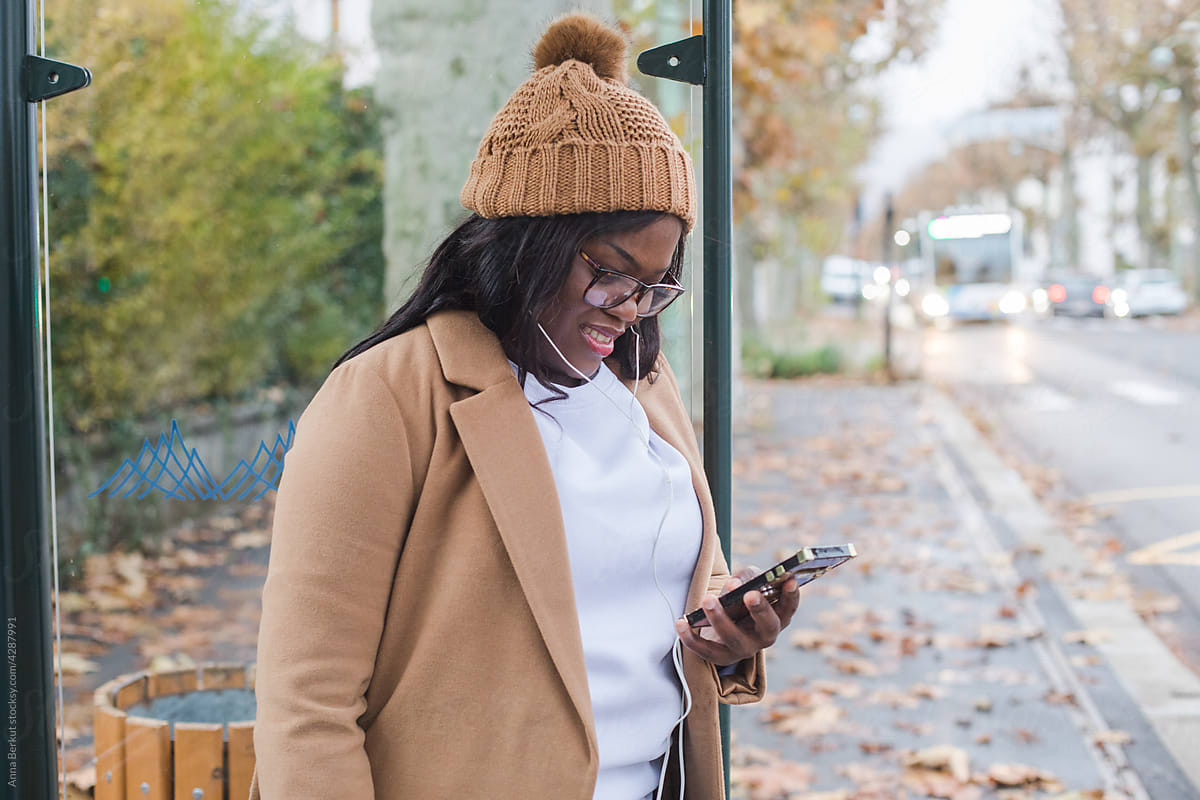 good news, smiling black woman using smartphone on bus stop