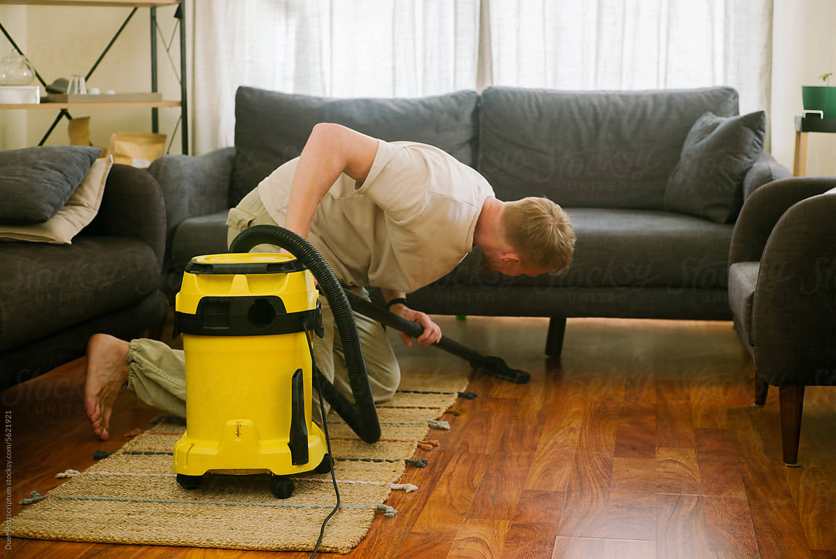 Blond-haired man vacuuming under the couch