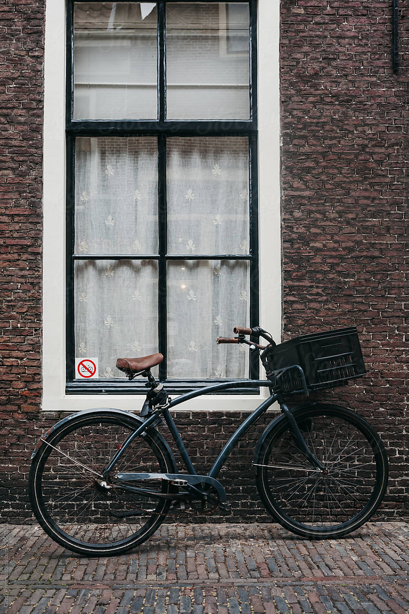 A bicycle parked against a window with a no parking sticker
