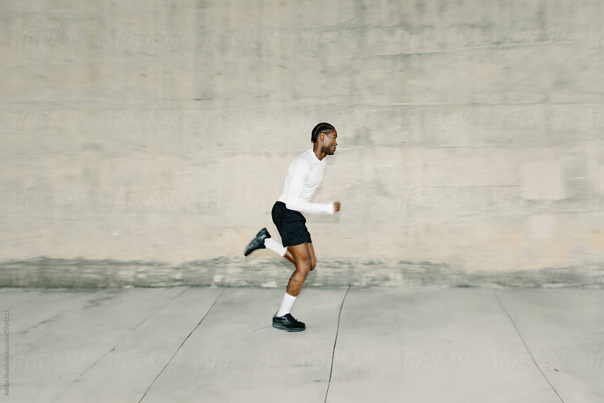 A black man performs sprints in a concrete alley
