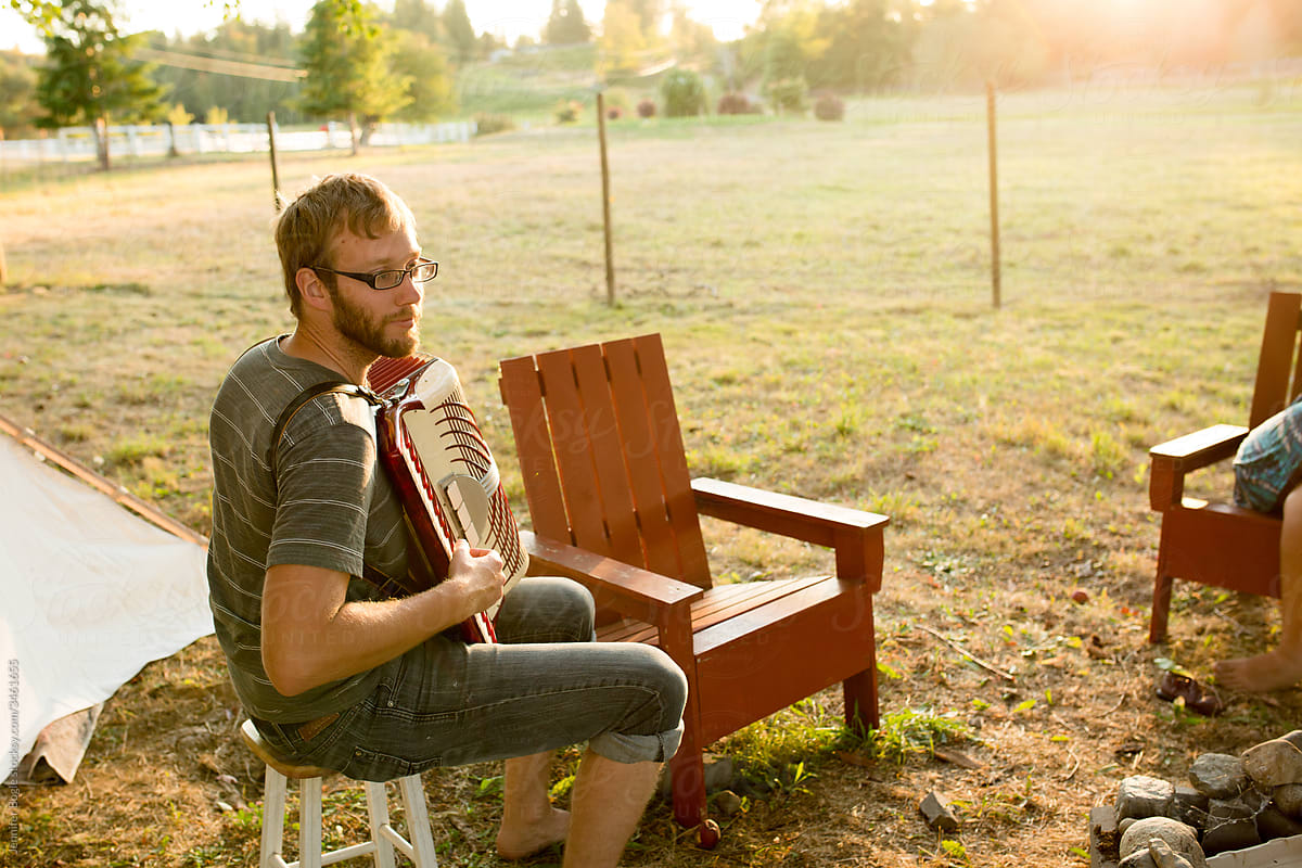 Bearded man playing accordion in sunny campsite
