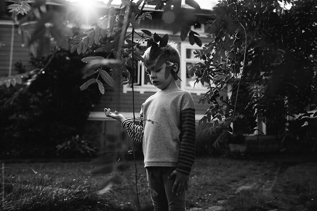 Young boy closes his eyes and holds his hand out while playing in a garden.