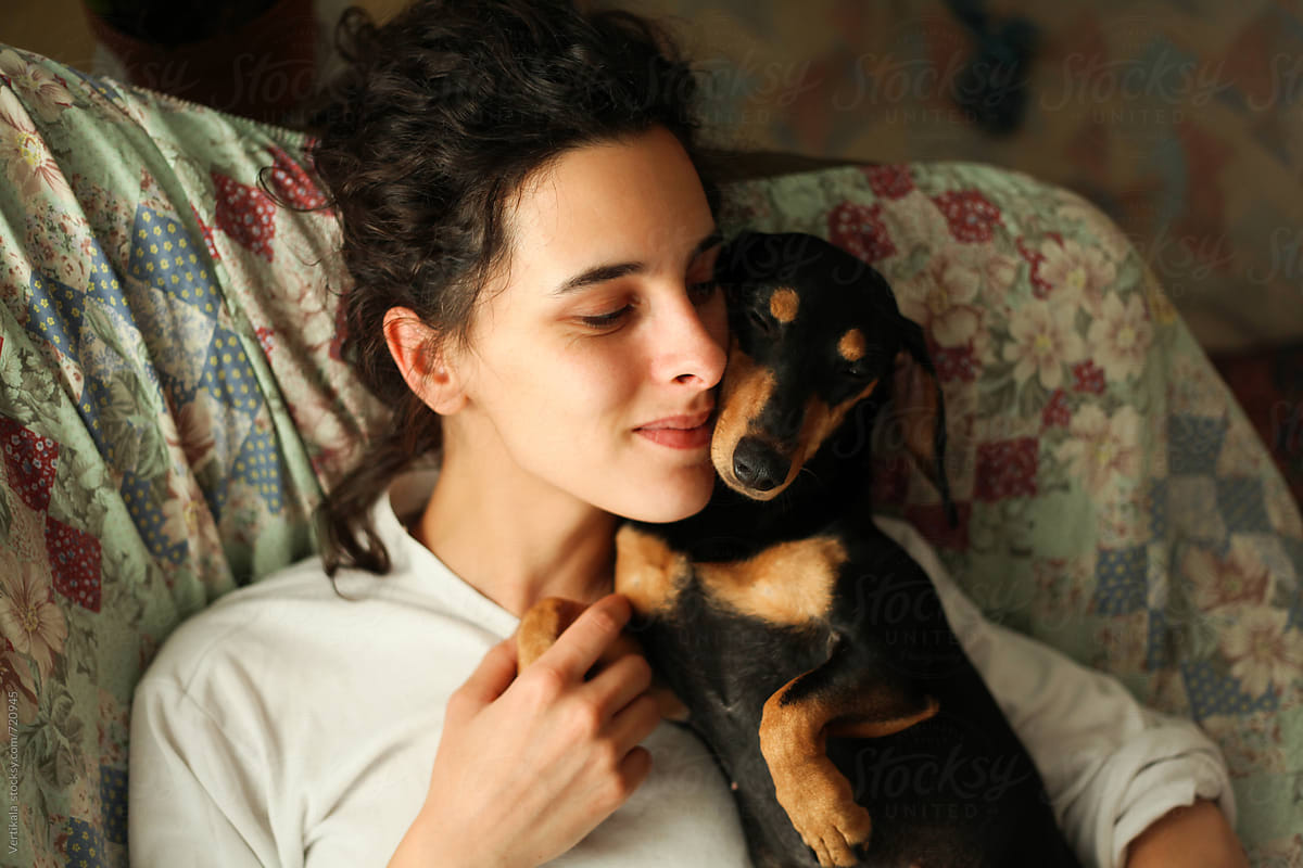 Young woman and her small black dog hugging on the couch. From above.