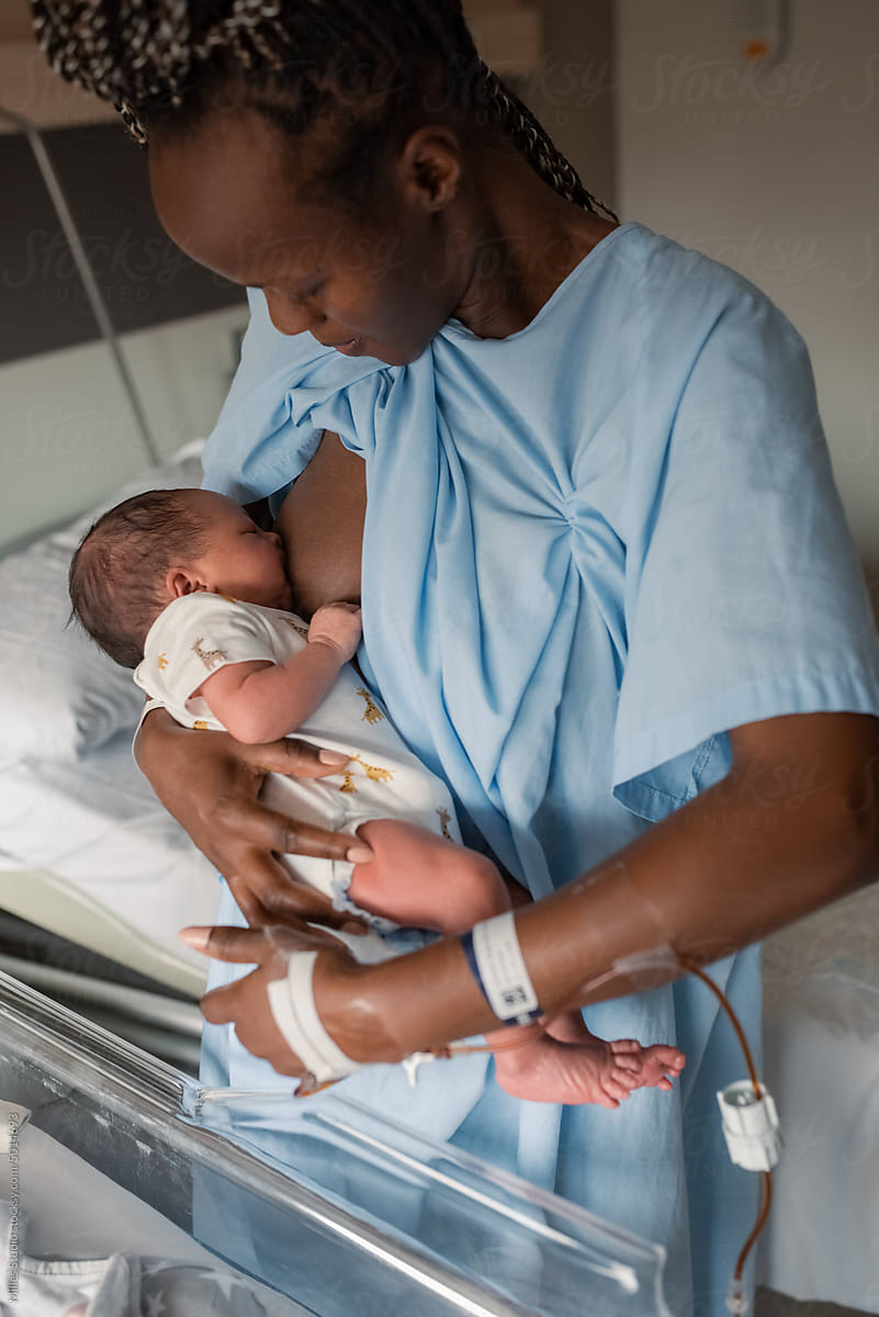 Black mom breastfeeding infant near medical crib